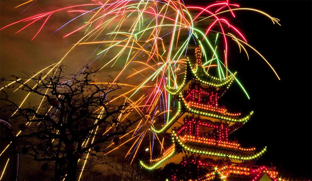 red, orange and green fireworks above a traditional Chinese house
